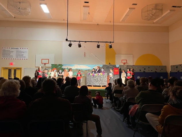 A group of children on a stage in a room with a crowd

Description automatically generated