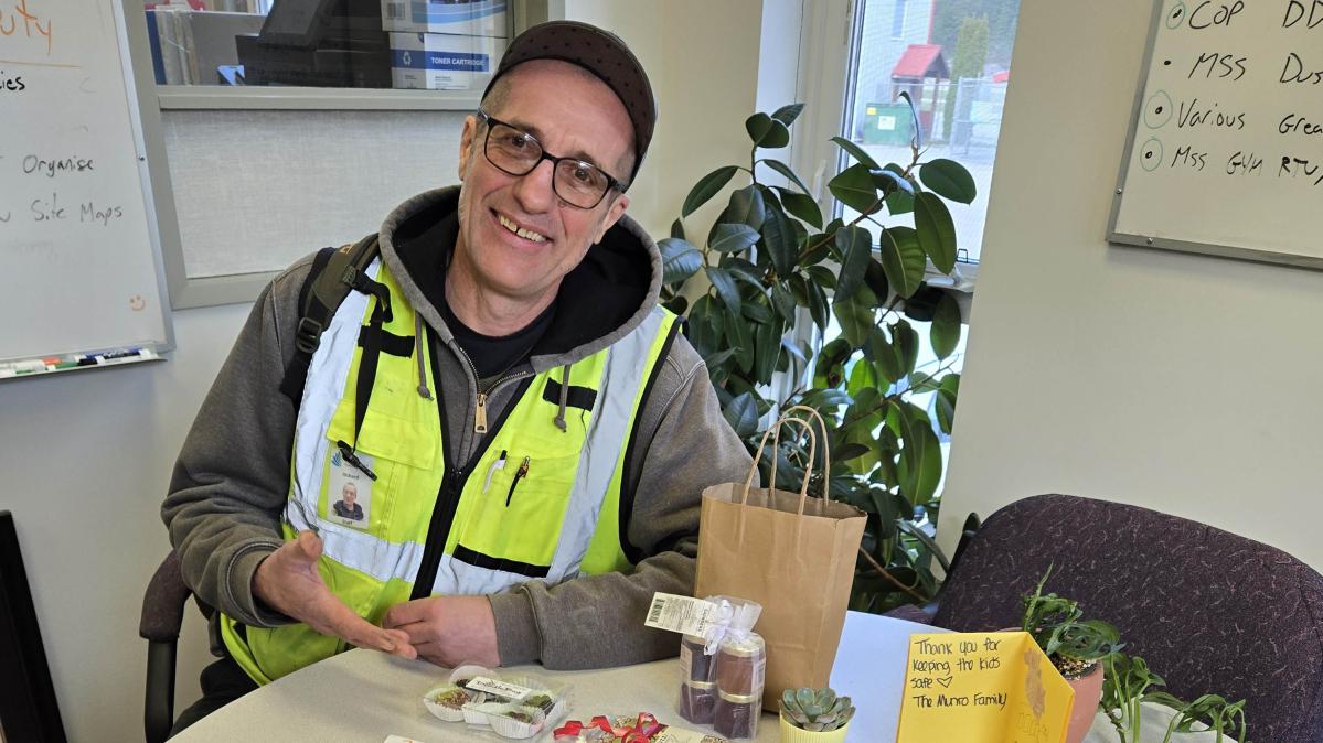 A man in a ball cap, glasses and a flourescent green vest sits at a table covered in hand-drawn cards and messages.